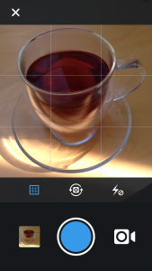 Nach dem Öffnen der App, wählt man das kleine Kamera-Symbol. Nun erscheint folgender Bildschirm. Der blaue Punkt ist der Auslöser. Mit der kleinen Kamera kann man in den Video-Modus wechseln. Darüber kann man das Raster ein-/ausschalten, die Kamera umschalten oder den Blitz ein-/ausschalten.